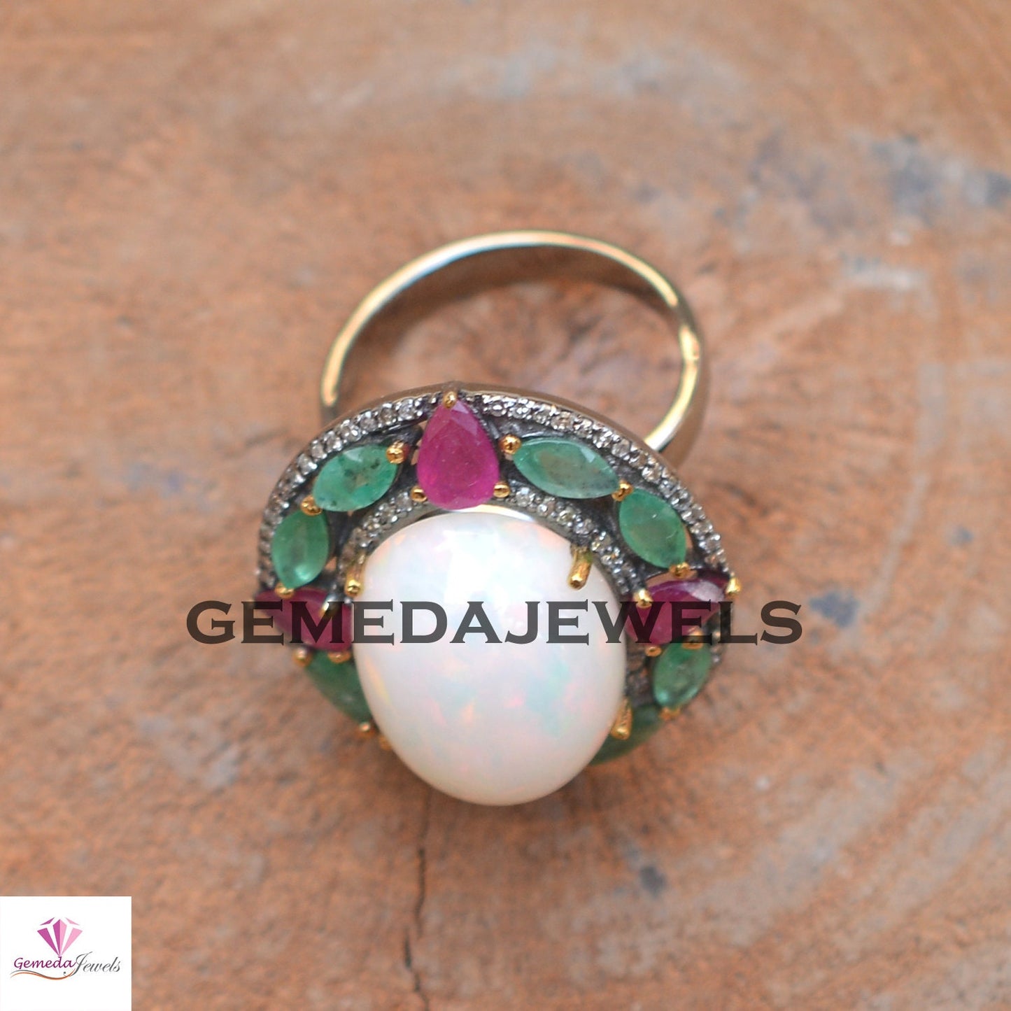 Decorative ring with a pearl and gemstones on a wooden surface, branded 'Gemedajewels'.